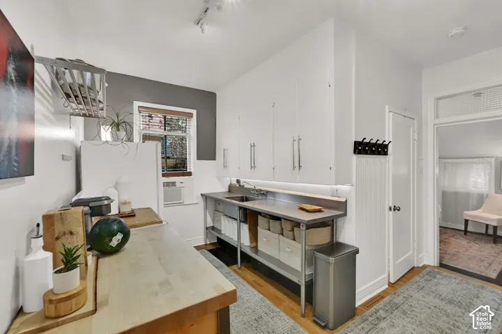 Kitchen featuring wood-finish flooring, white cabinetry with silver-tone pulls, stainless steel shelving and sink, and a contrasting gray accent wall