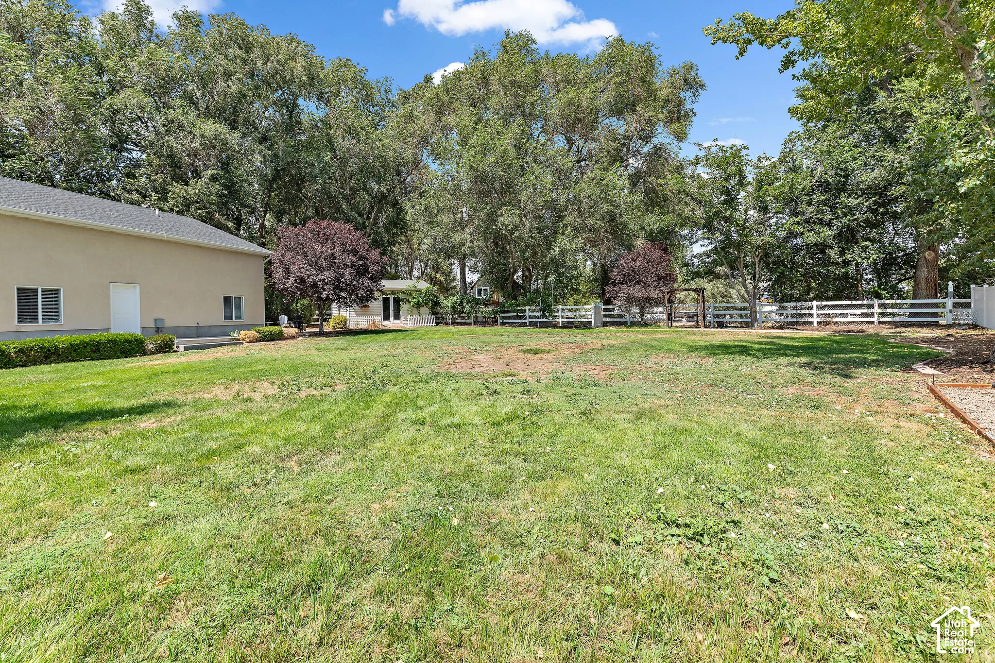Expansive lawn area with mature perimeter trees, complemented by a white picket fence and a separate accessory building