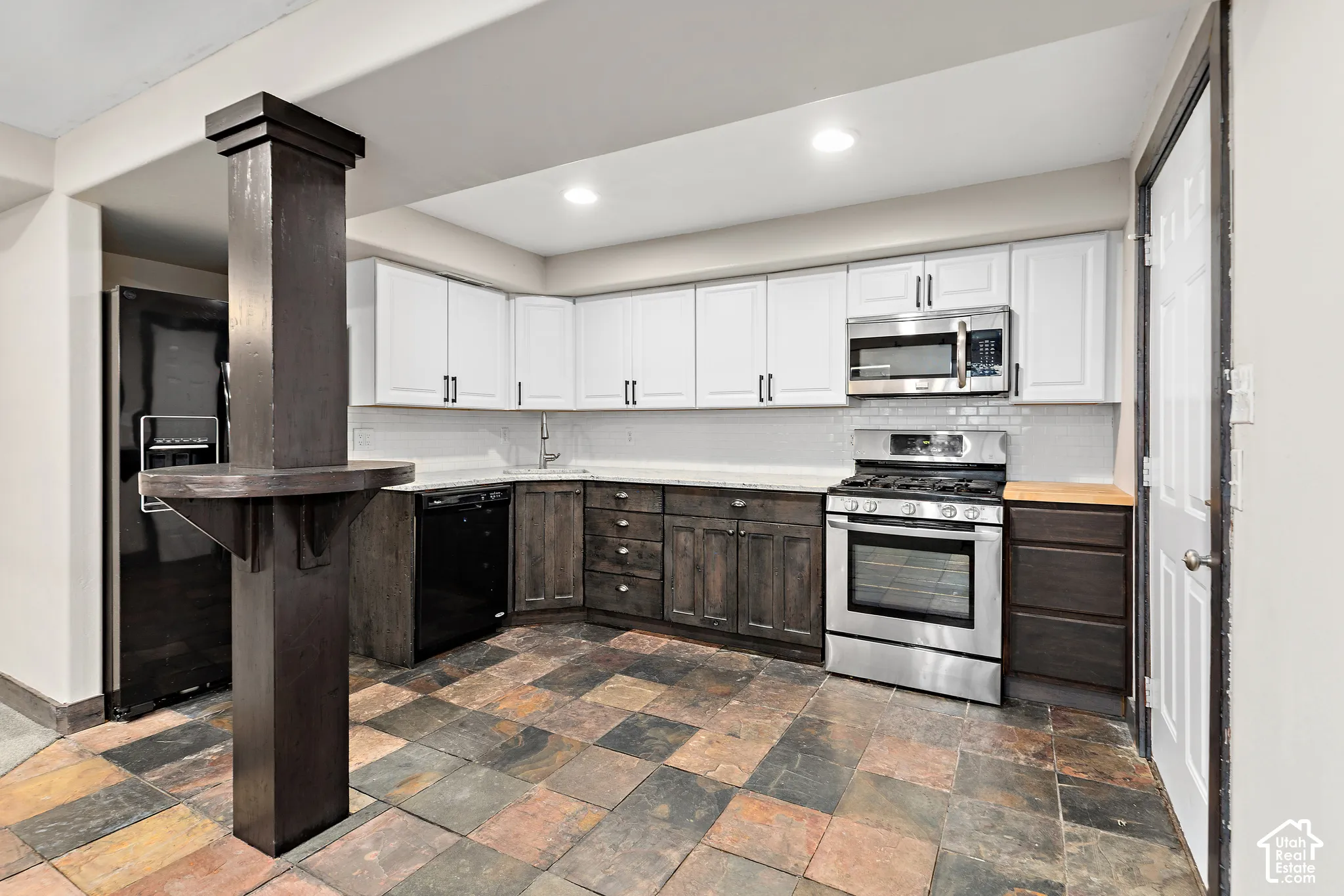 FLEX LIVING basement kitchen featuring a corner sink, white upper cabinetry, dark lower cabinetry, stainless steel appliances, and a tiled backsplash
