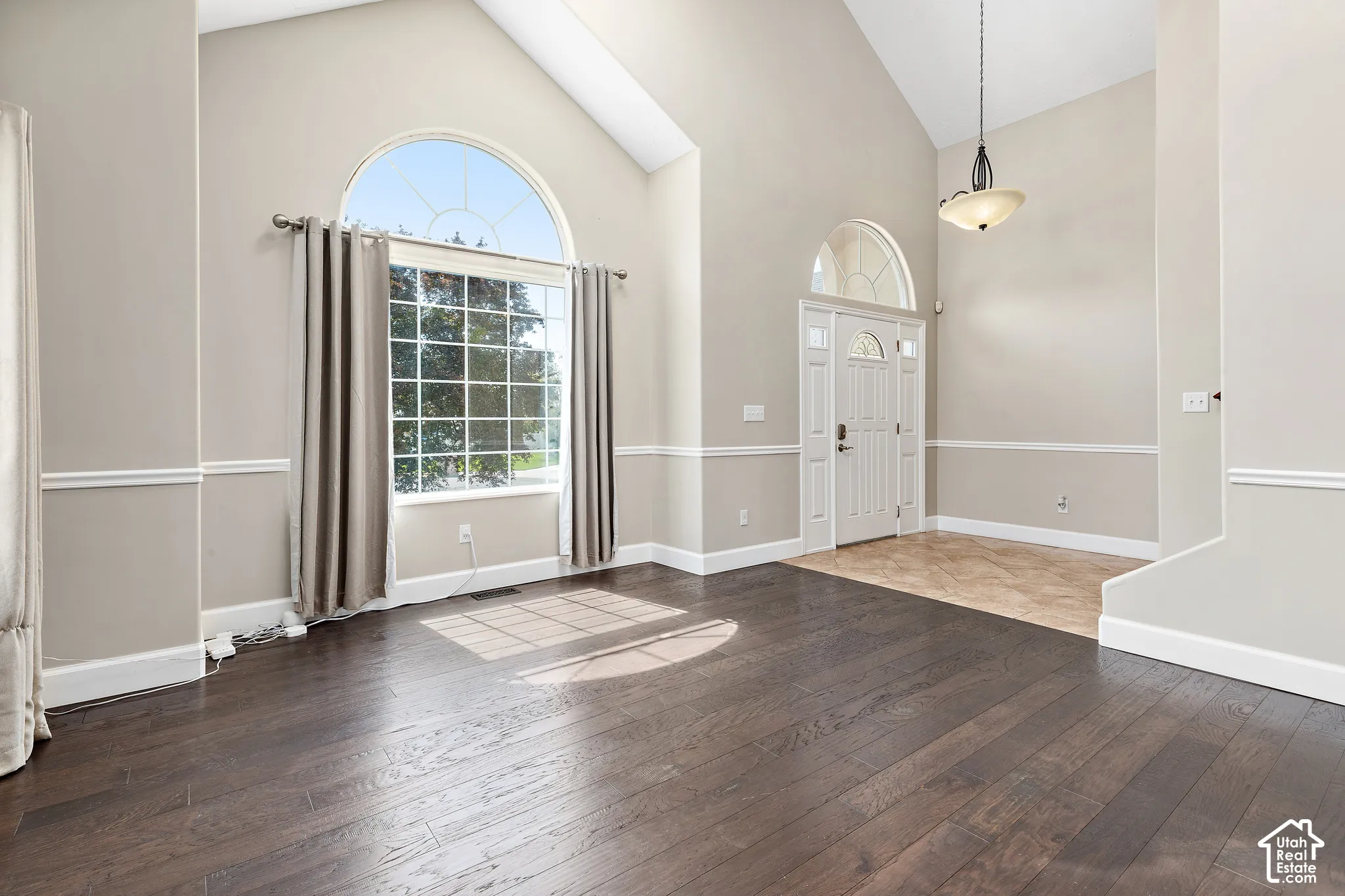 Vaulted ceilings, large arched window, dark wood-finish flooring, white paneled entry door with transom, and decorative pendant light fixture
