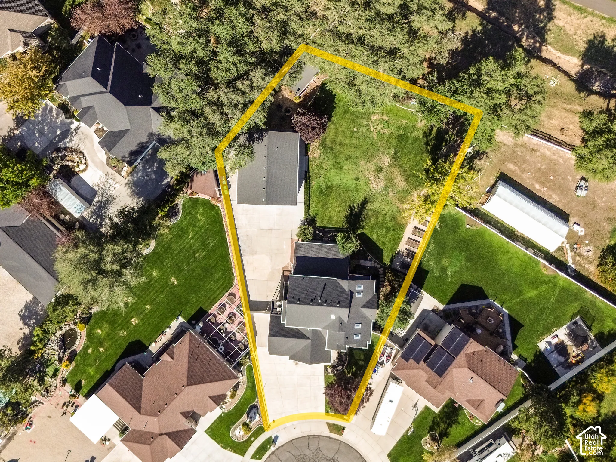 Aerial perspective of the lot featuring a sprawling lawn, mature trees, a detached heated RV garage, and a concrete driveway