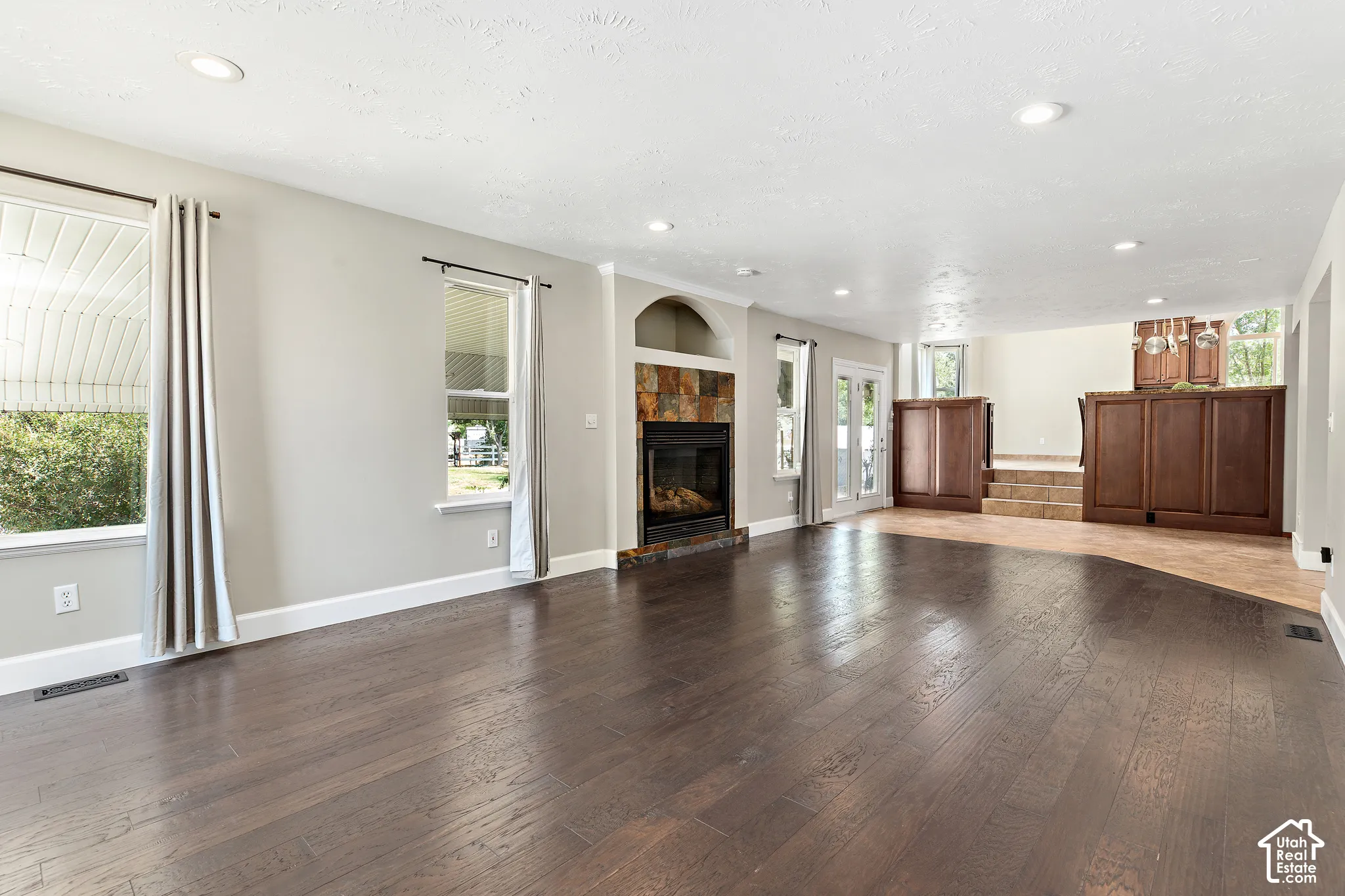 Expansive living space featuring rich wood-finish flooring, a stone-faced fireplace, recessed lighting, and bright windows