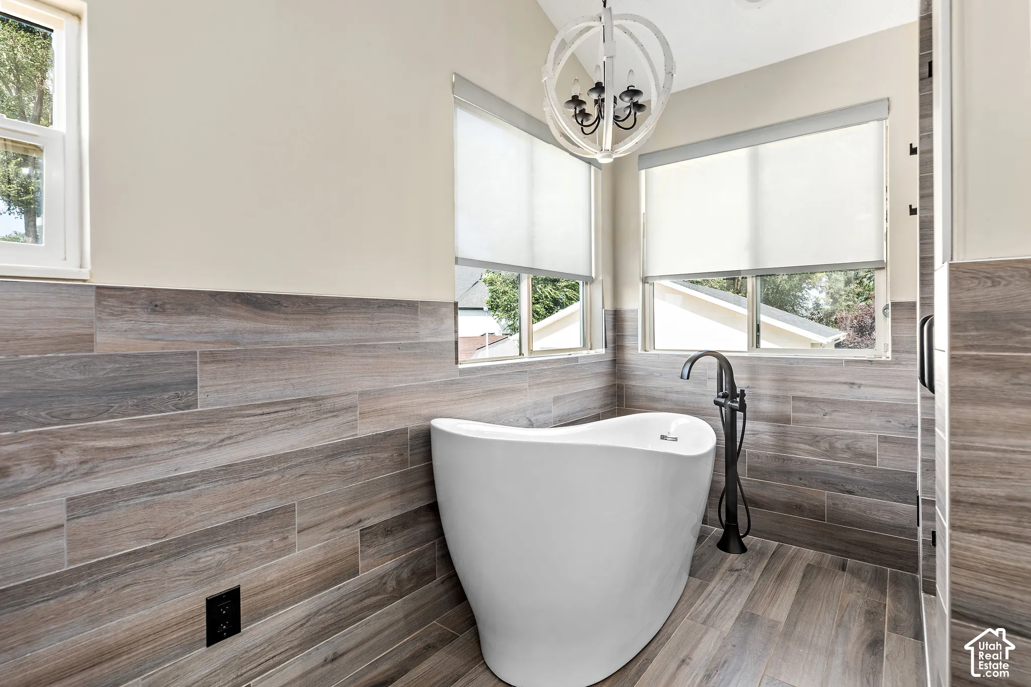 Primary freestanding soaking tub with a floor-mounted matte black faucet, surrounded by wood-finish tile flooring and wainscoting