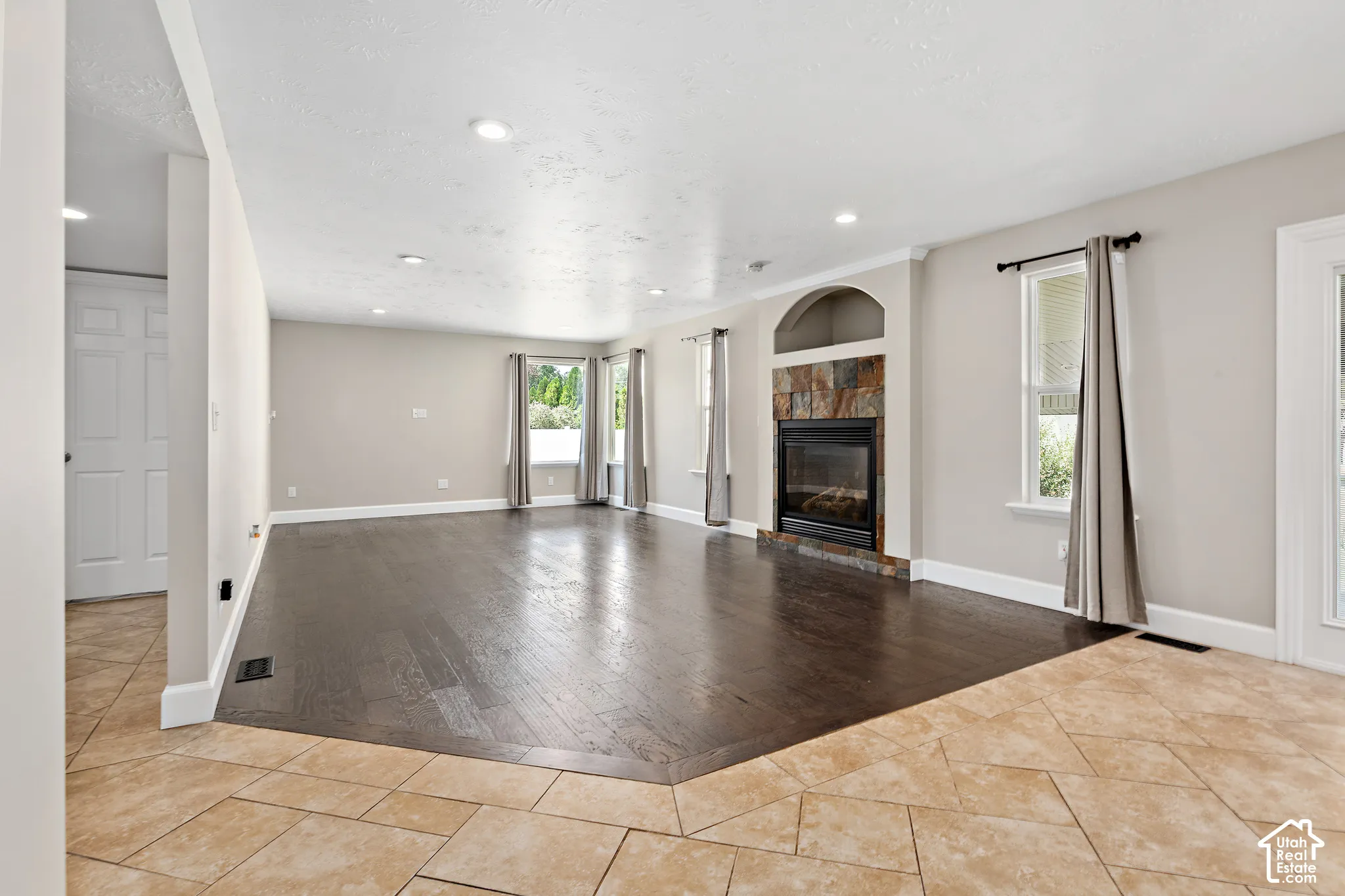 Recessed lighting throughout, stone-surround fireplace with arched alcove, wood-finish flooring, tiled entry, and multiple windows