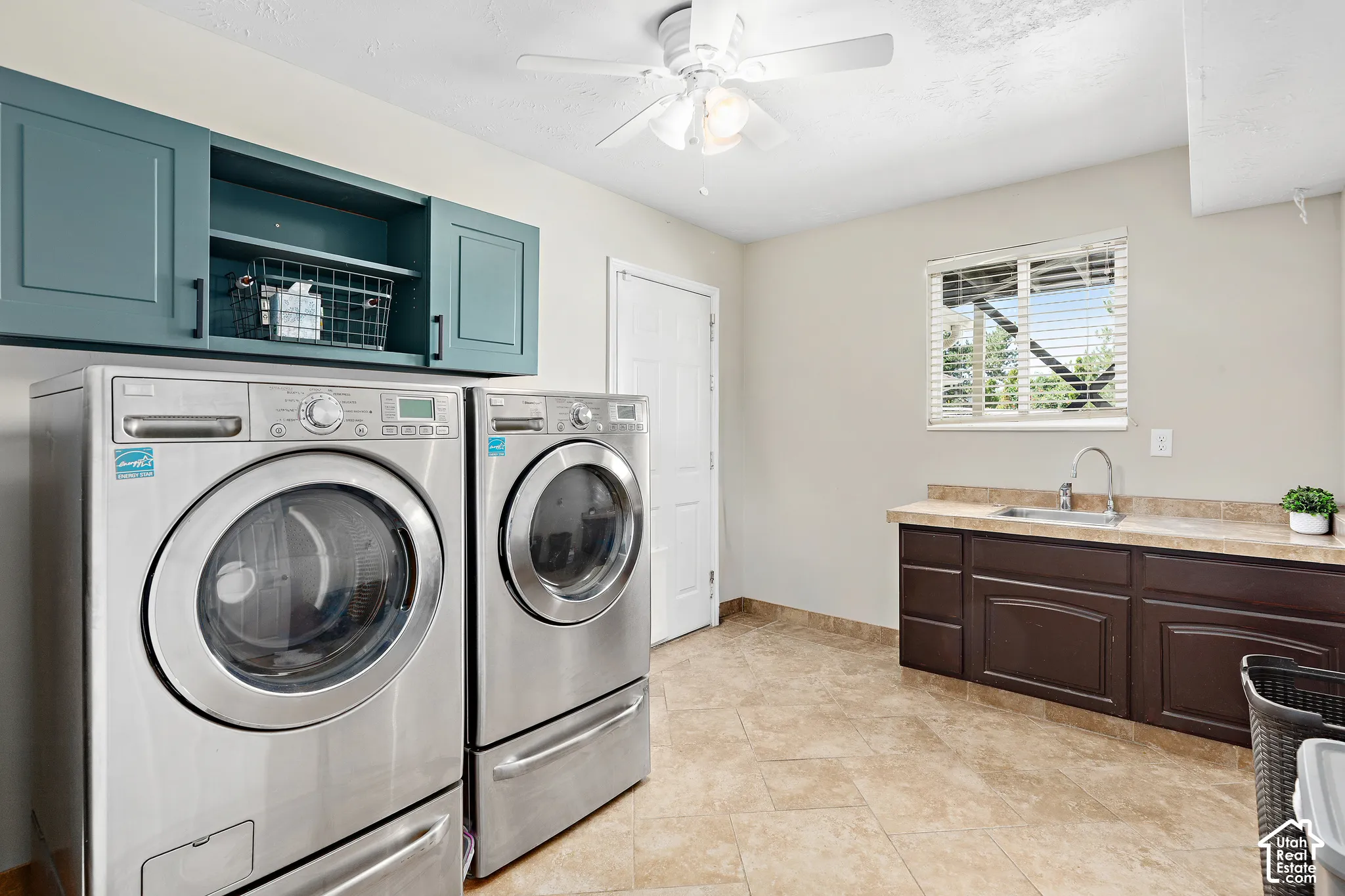 Ceramic tile flooring throughout, featuring an included washer and dryer, a utility sink, a window with blinds, and an exit to the three-car garage