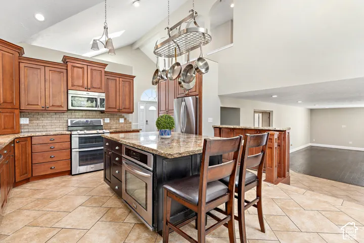 Kitchen featuring wood cabinetry, stainless steel appliances, a center island with an integrated oven, tile flooring, and a pot rack