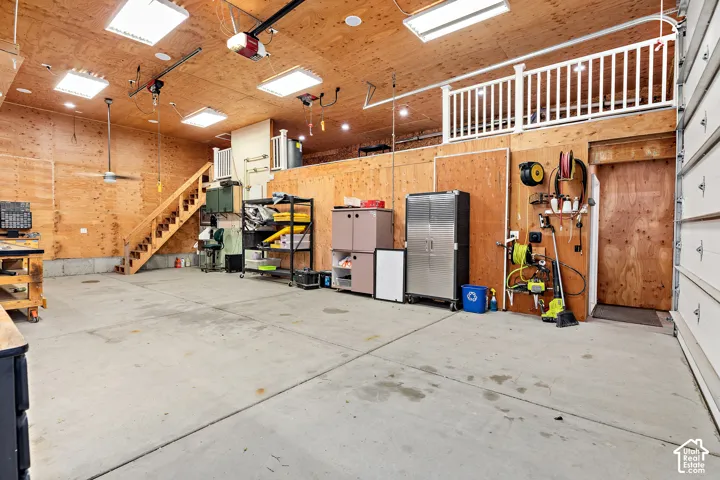 Spacious garage with wood-paneled walls and ceiling, concrete flooring, and an elevated loft area with a white railing