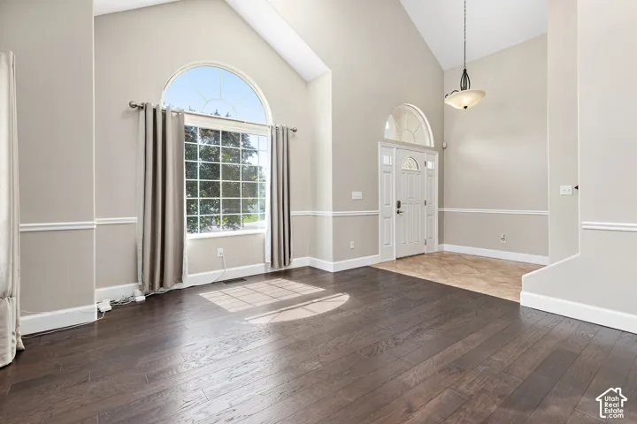 Vaulted ceilings, large arched window, dark wood-finish flooring, white paneled entry door with transom, and decorative pendant light fixture