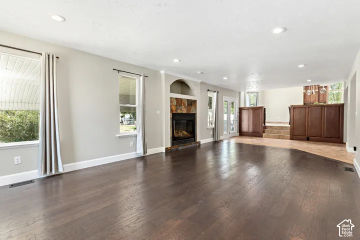 Expansive living space featuring rich wood-finish flooring, a stone-faced fireplace, recessed lighting, and bright windows