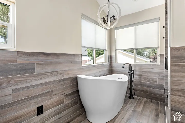 Primary freestanding soaking tub with a floor-mounted matte black faucet, surrounded by wood-finish tile flooring and wainscoting