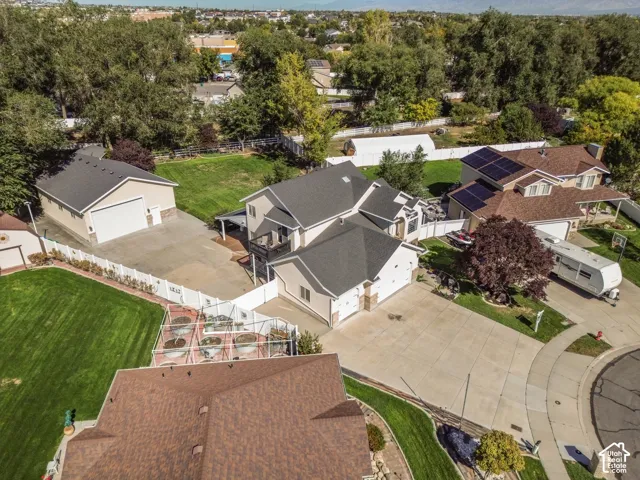 Aerial perspective featuring a multi-structure property with an attached multi-car garage, a detached garage, manicured lawn, white vinyl fencing, and a fenced garden area