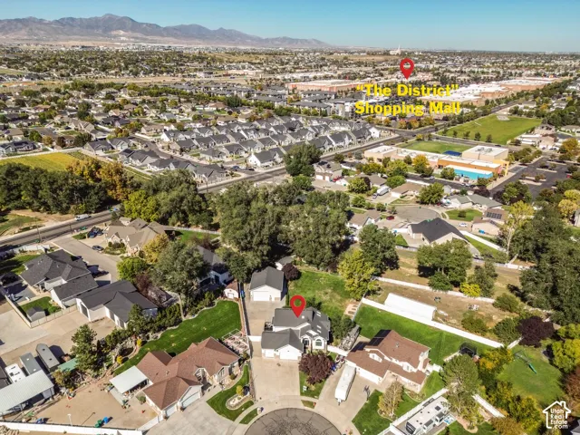 Aerial perspective of a multi-level residential property featuring a multi-car garage, expansive private lawn, mature landscaping, and a mountain range backdrop