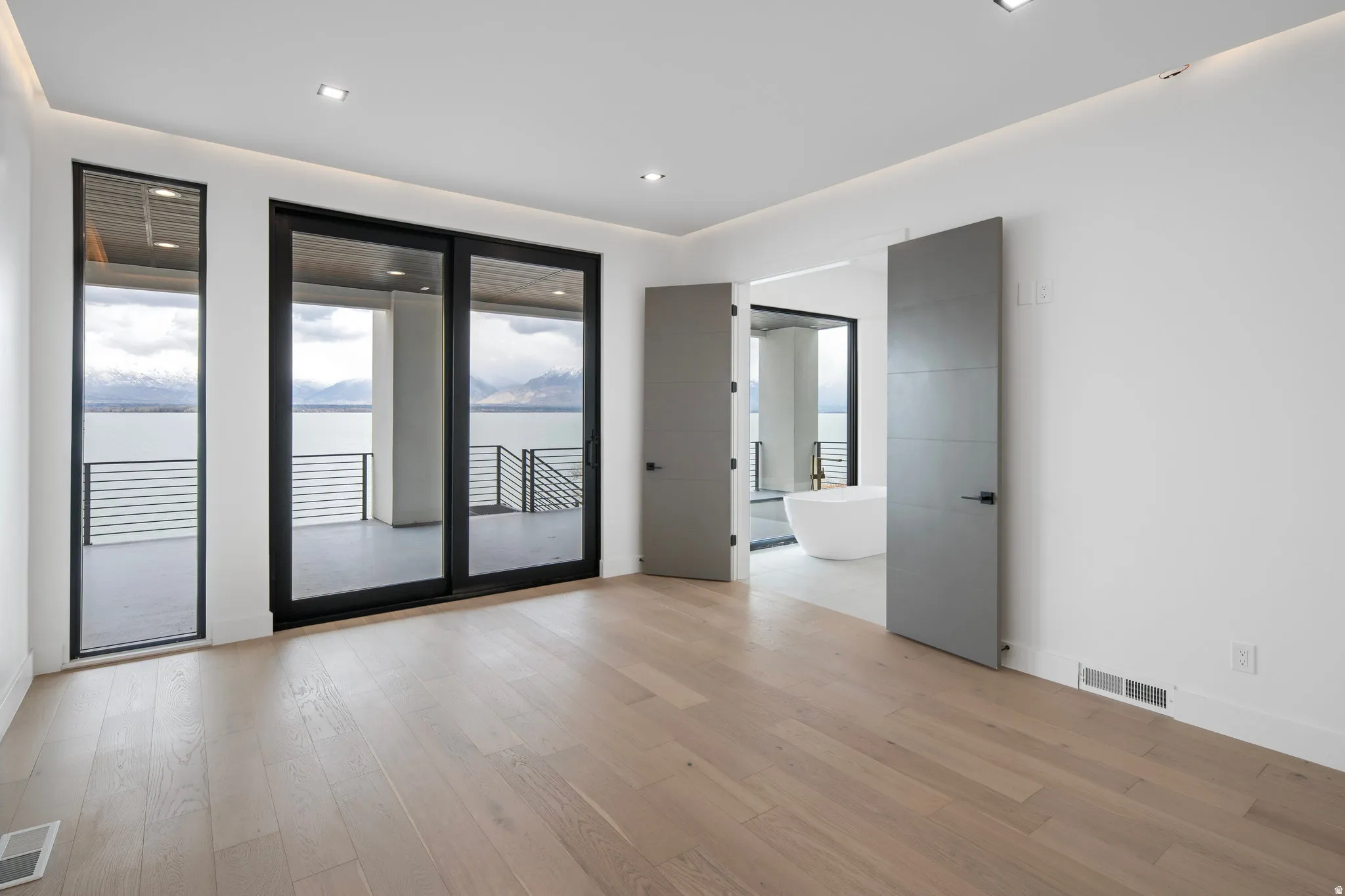 Recessed ceiling lighting, wood-finish flooring, sliding glass doors, balcony access, and a freestanding soaking tub