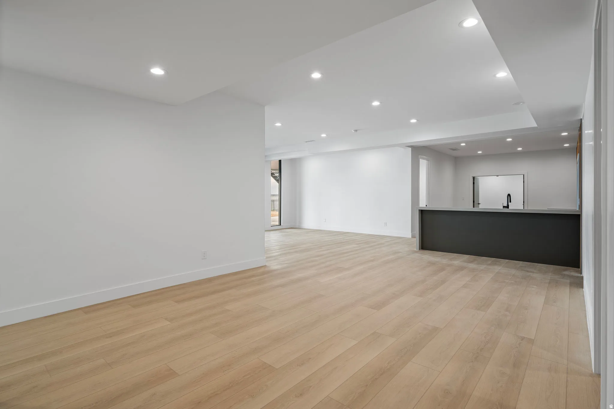 Open-concept living space featuring light wood-finish flooring, recessed lighting, and a built-in bar with a dark base and light countertop