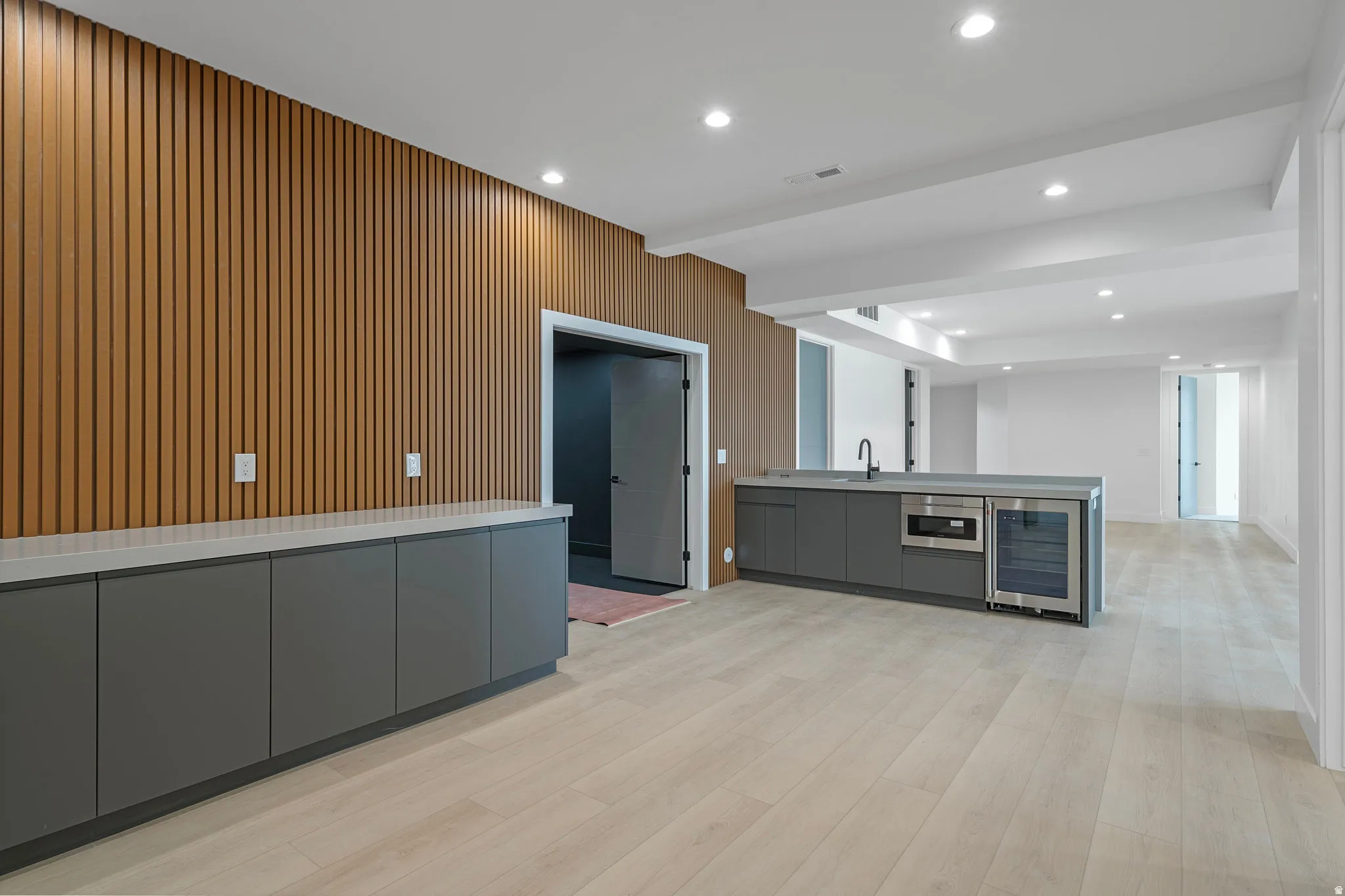 Wood-finish slat wall accent, recessed lighting, wood-finish flooring, built-in cabinetry with light-toned countertops, and an integrated beverage cooler