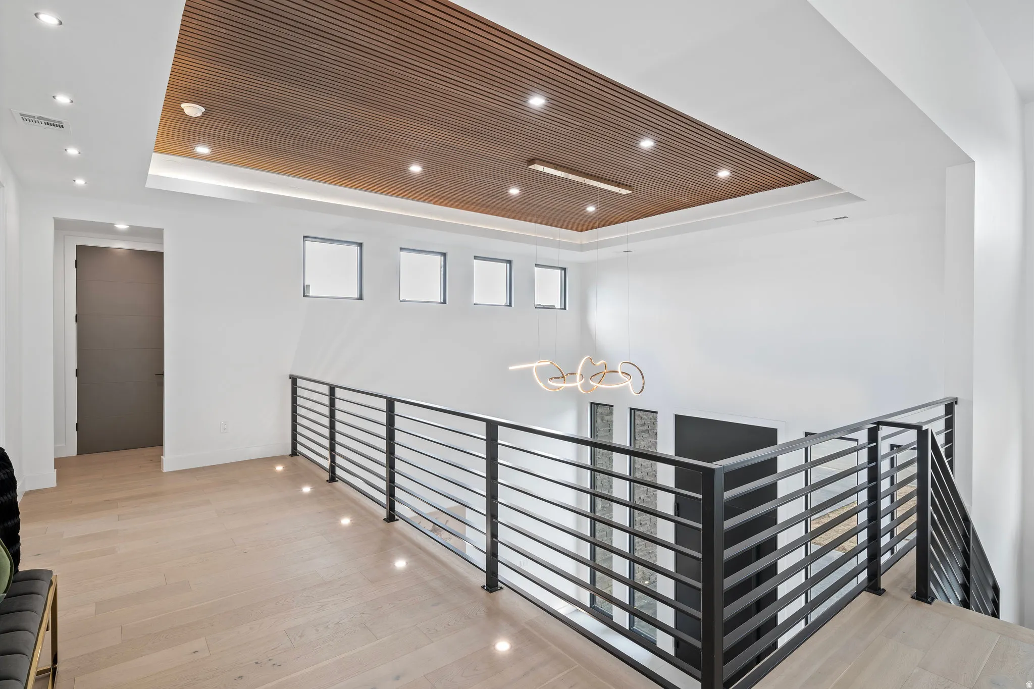 Wood-finish flooring, contemporary black metal railings, recessed lighting, wood-paneled ceiling accent, and a modern chandelier