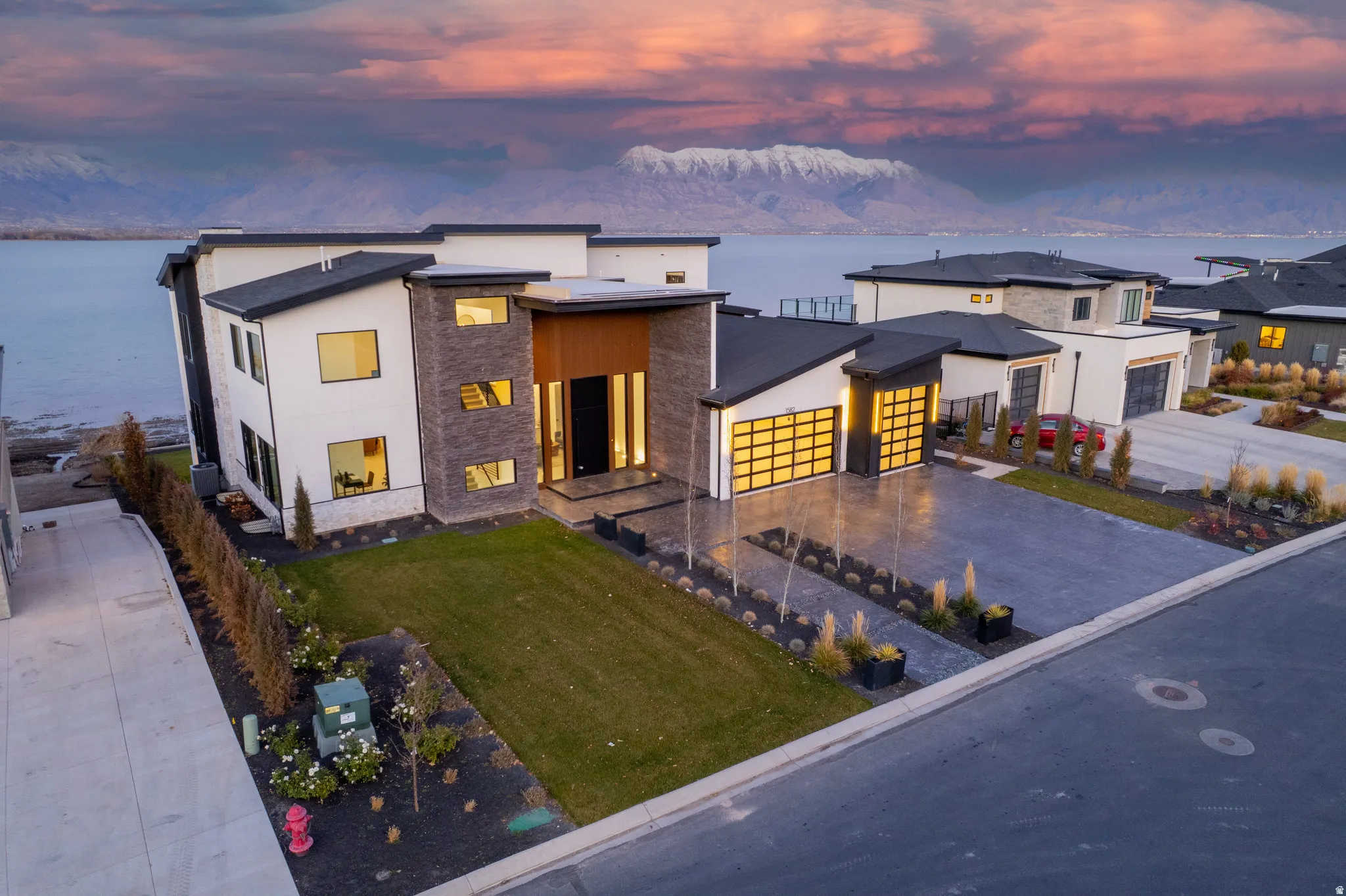 Modern architecture featuring a multi-tone facade, expansive windows, a two-car garage with translucent doors, and a paved driveway
