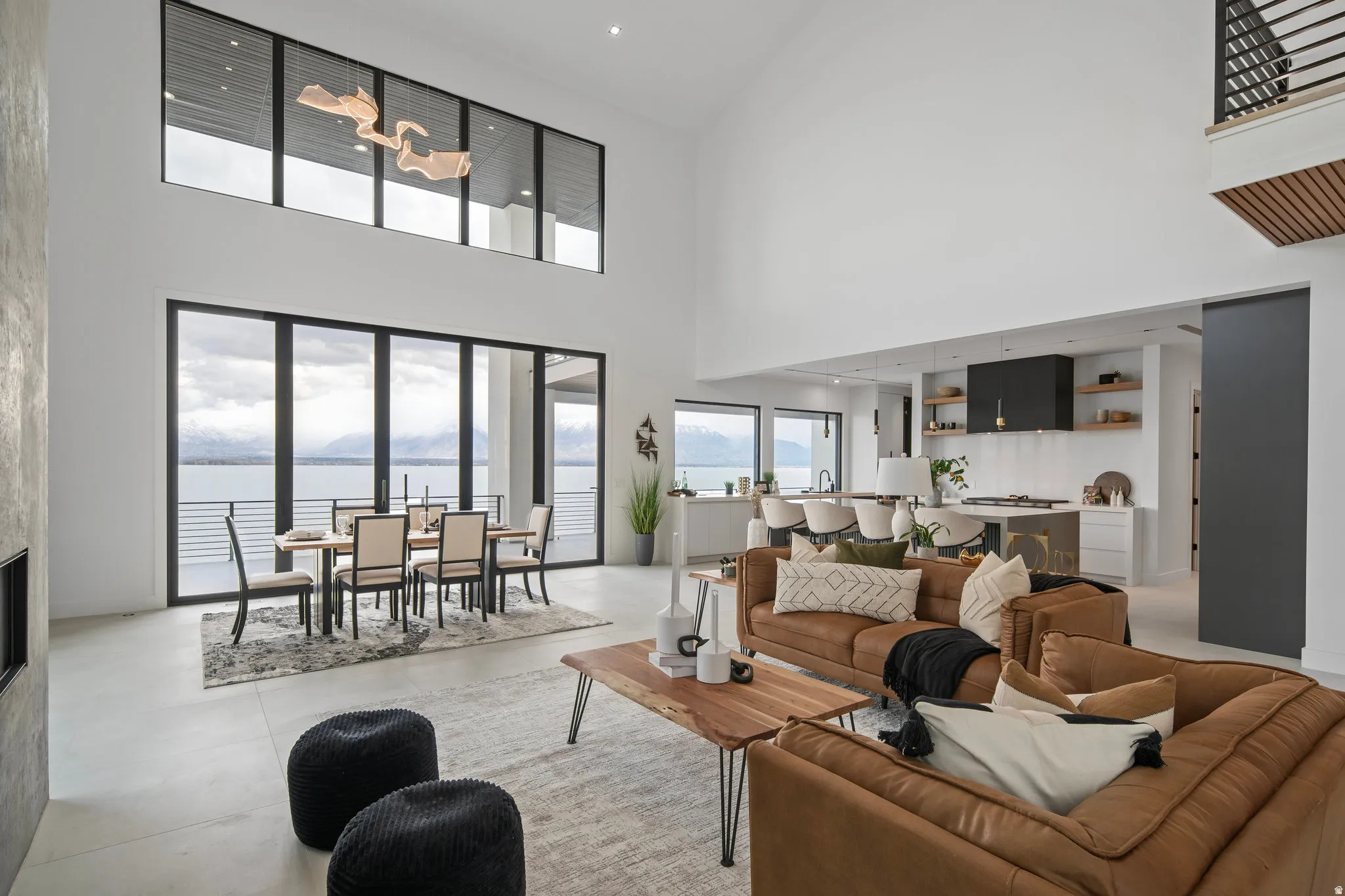 Two-story living area with expansive floor-to-ceiling windows, integrated fireplace, open-concept kitchen, and a decorative pendant light fixture