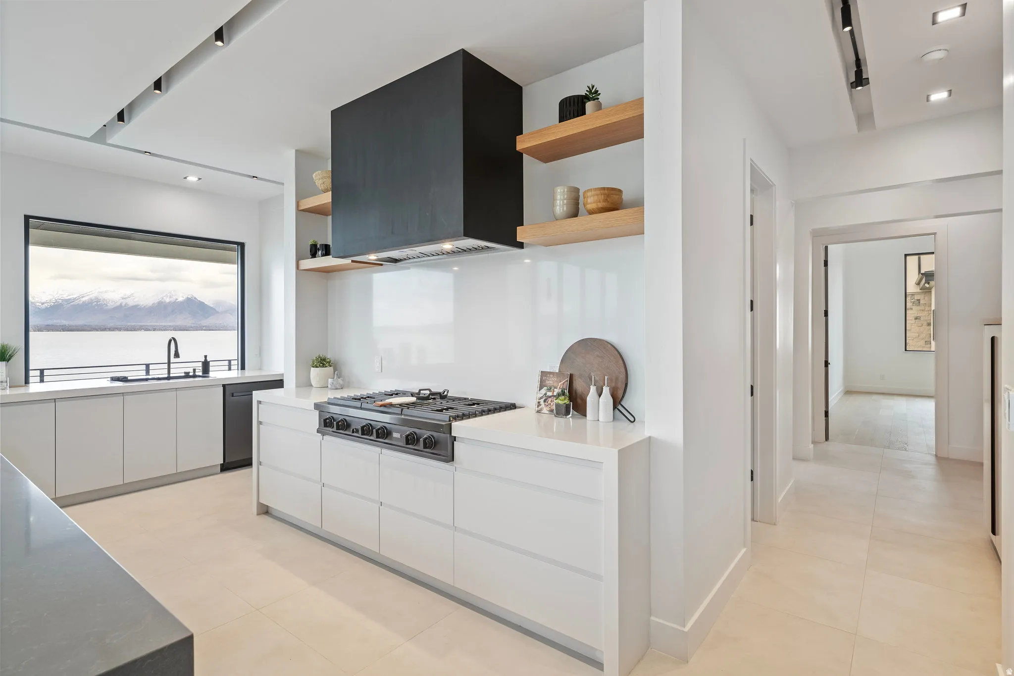 Modern kitchen featuring a large picture window, white cabinetry, integrated range with a black hood, and light-toned tile flooring
