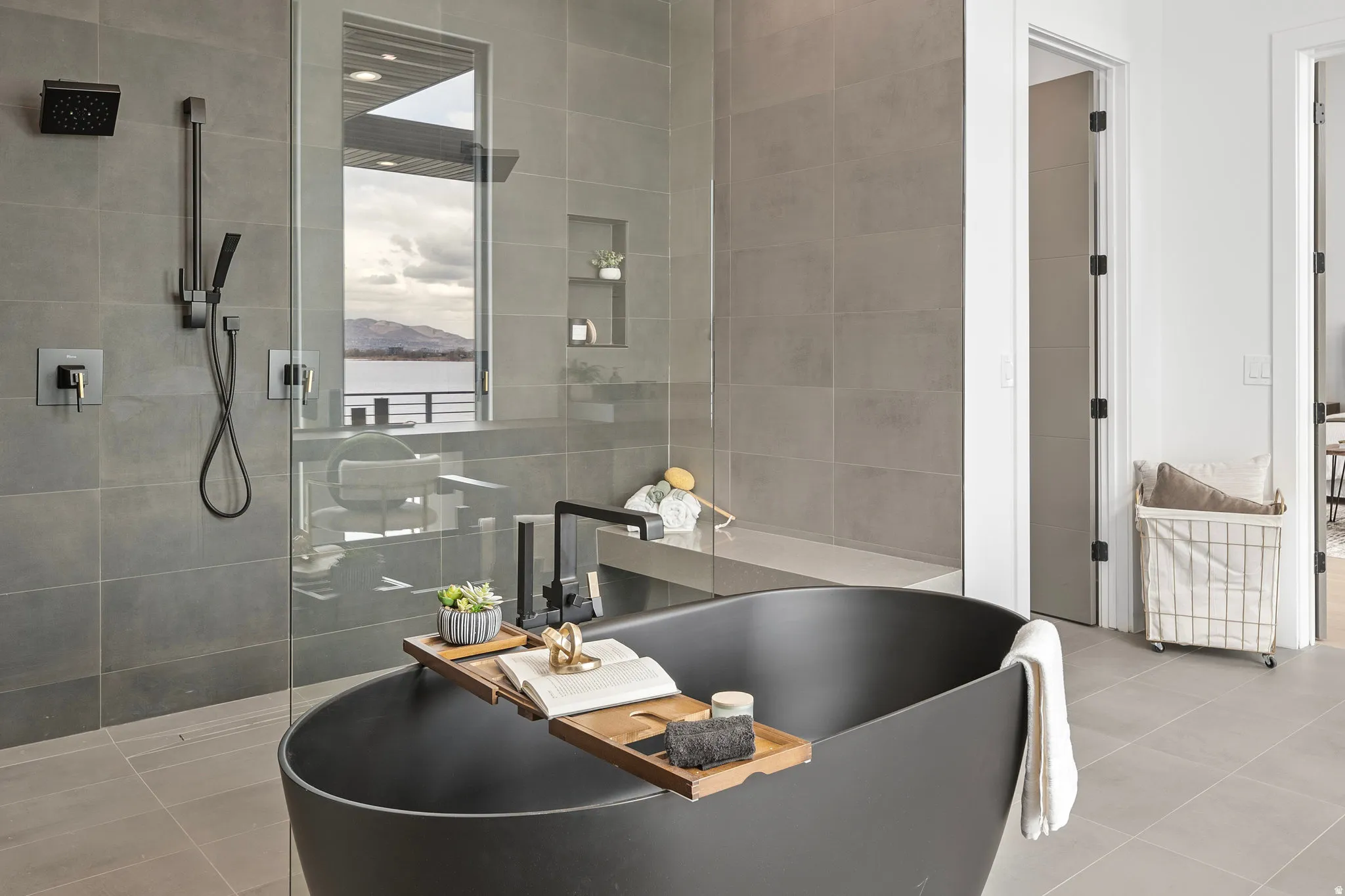 Freestanding matte black soaking tub, enclosed shower with a built-in bench, large format tile walls, and a window with a water backdrop