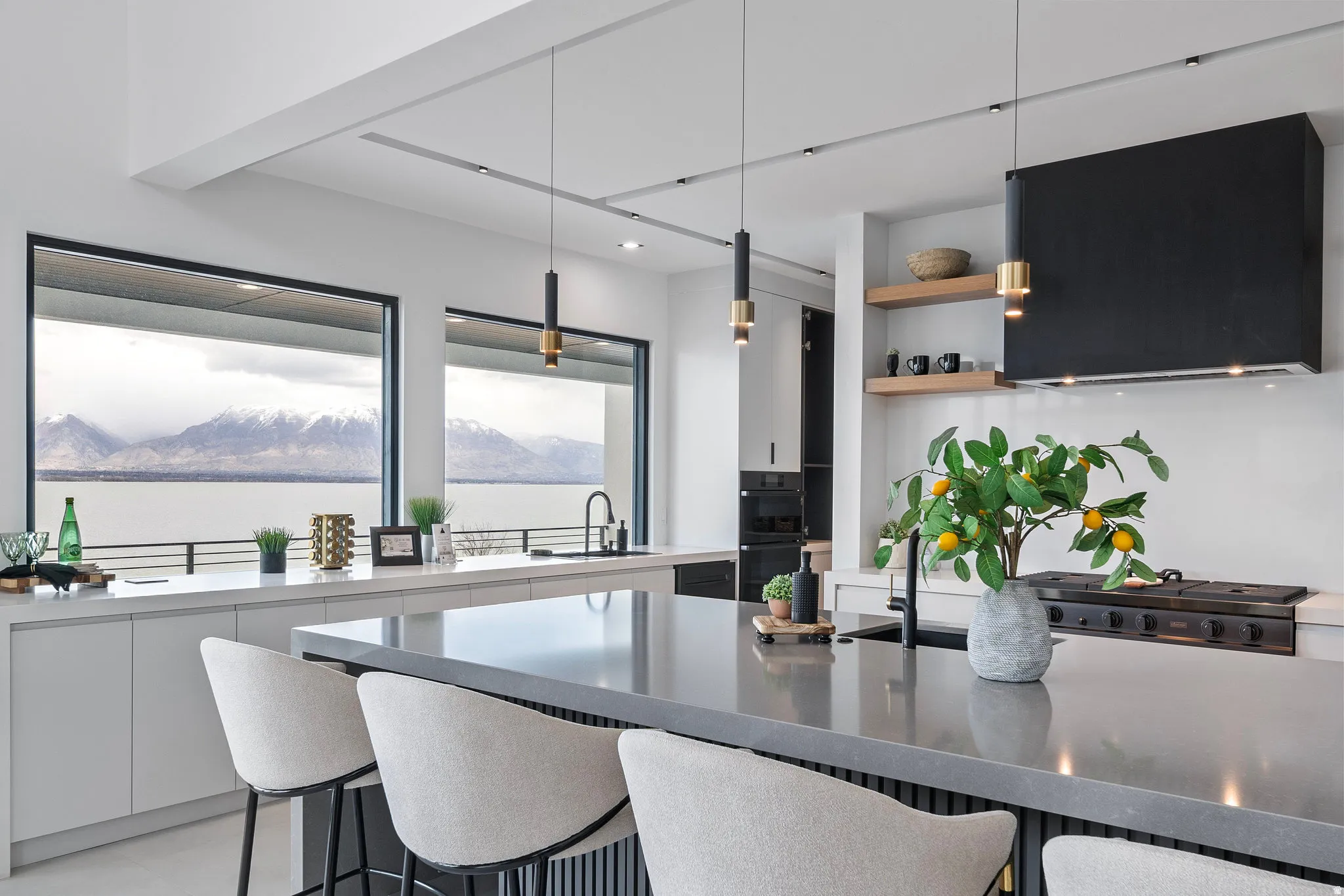 Expansive kitchen island with seating, panoramic windows, built-in stainless steel appliances, custom range hood, and open shelving
