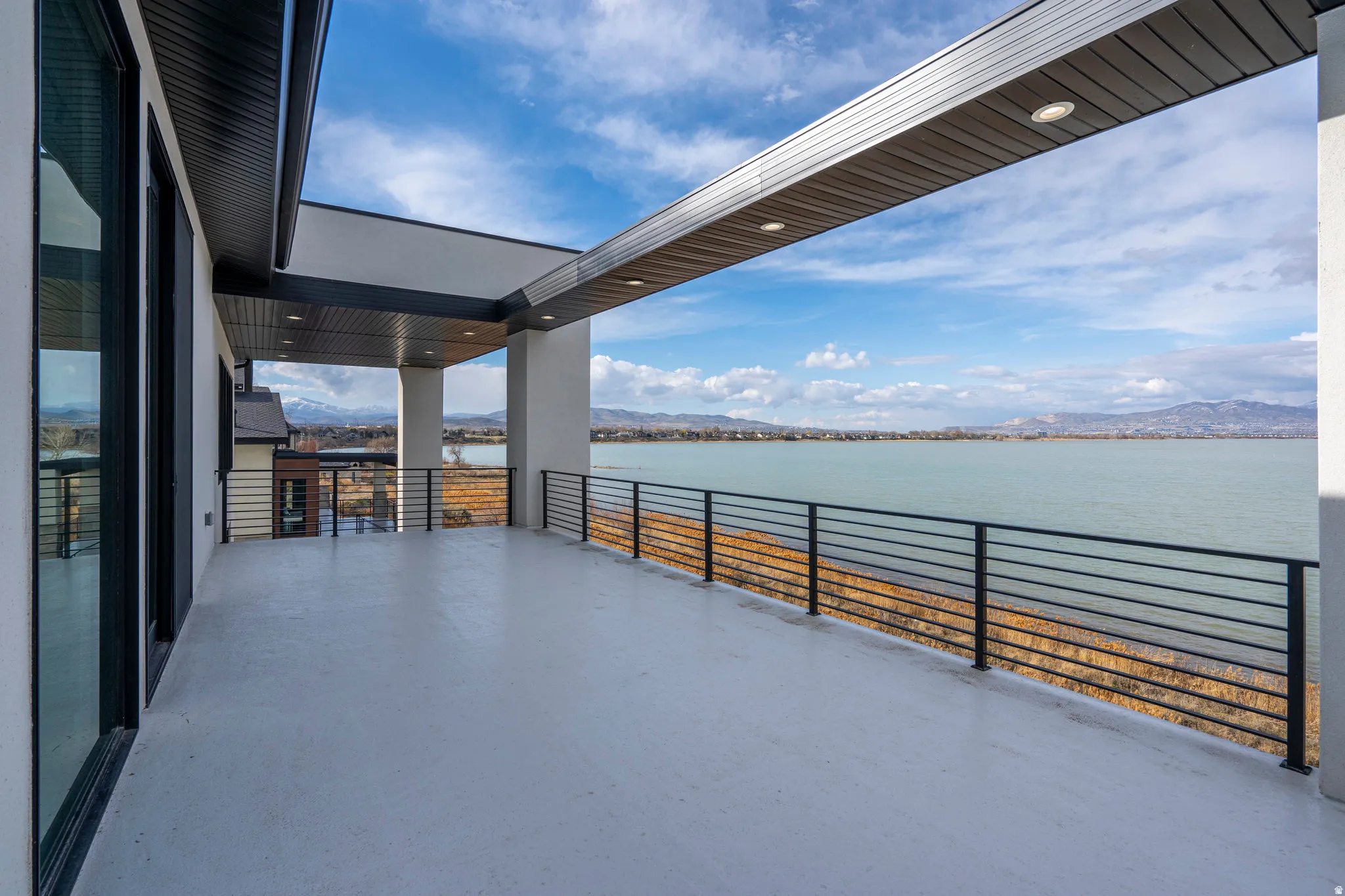 Expansive outdoor deck with a concrete surface, black metal horizontal railings, and a covered ceiling with recessed lighting
