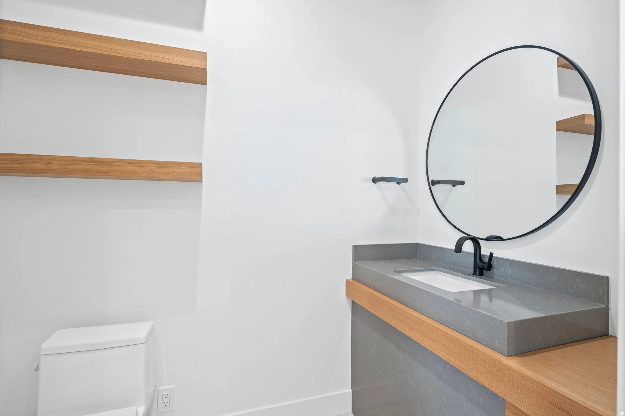 Floating wood shelves, a circular black-framed mirror, and a contemporary vanity with an integrated sink and matte black faucet