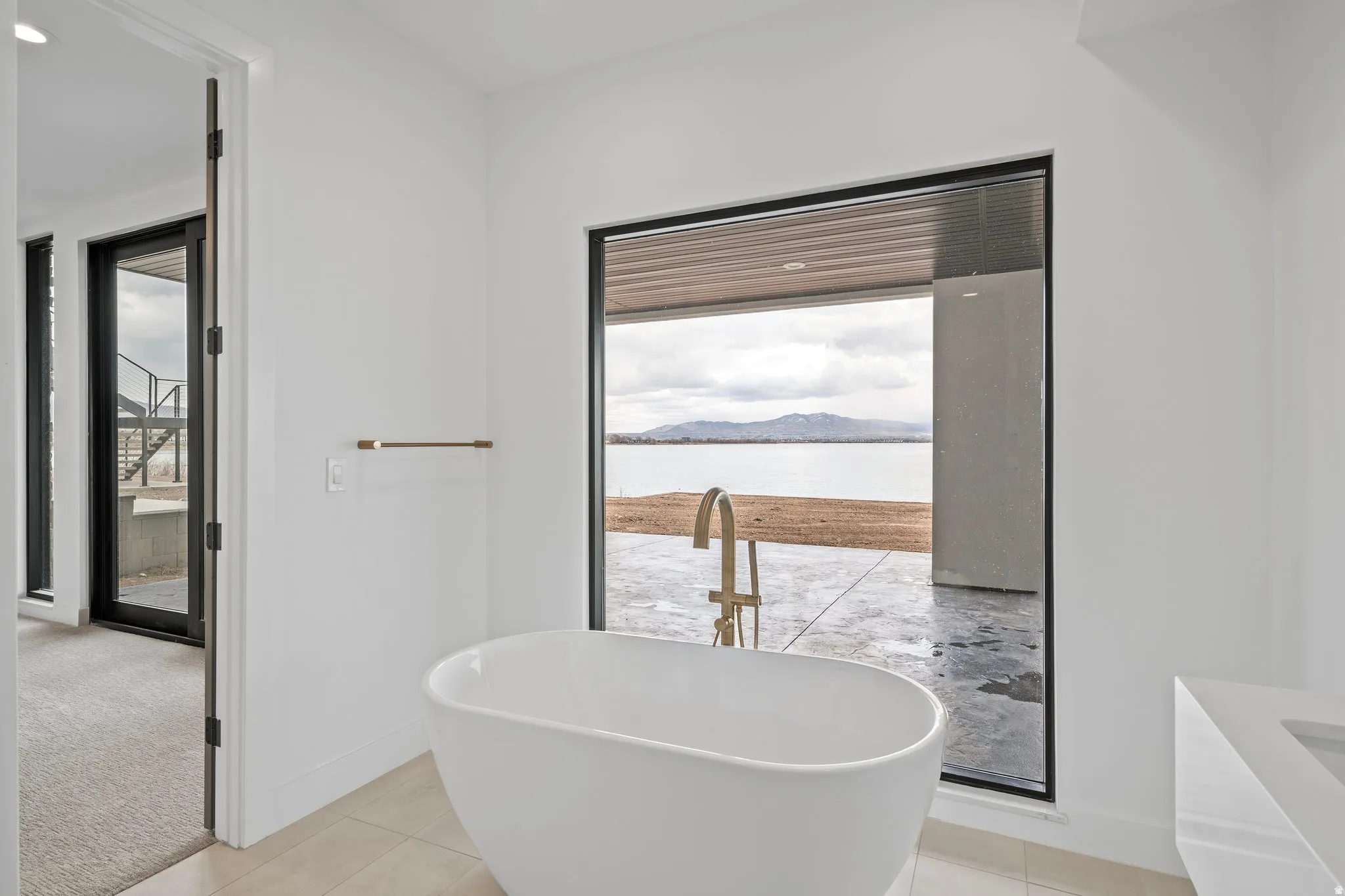 Freestanding soaking tub with a floor-mounted gold-finish faucet, large picture window with mountain scenery, and a white vanity with an integrated basin