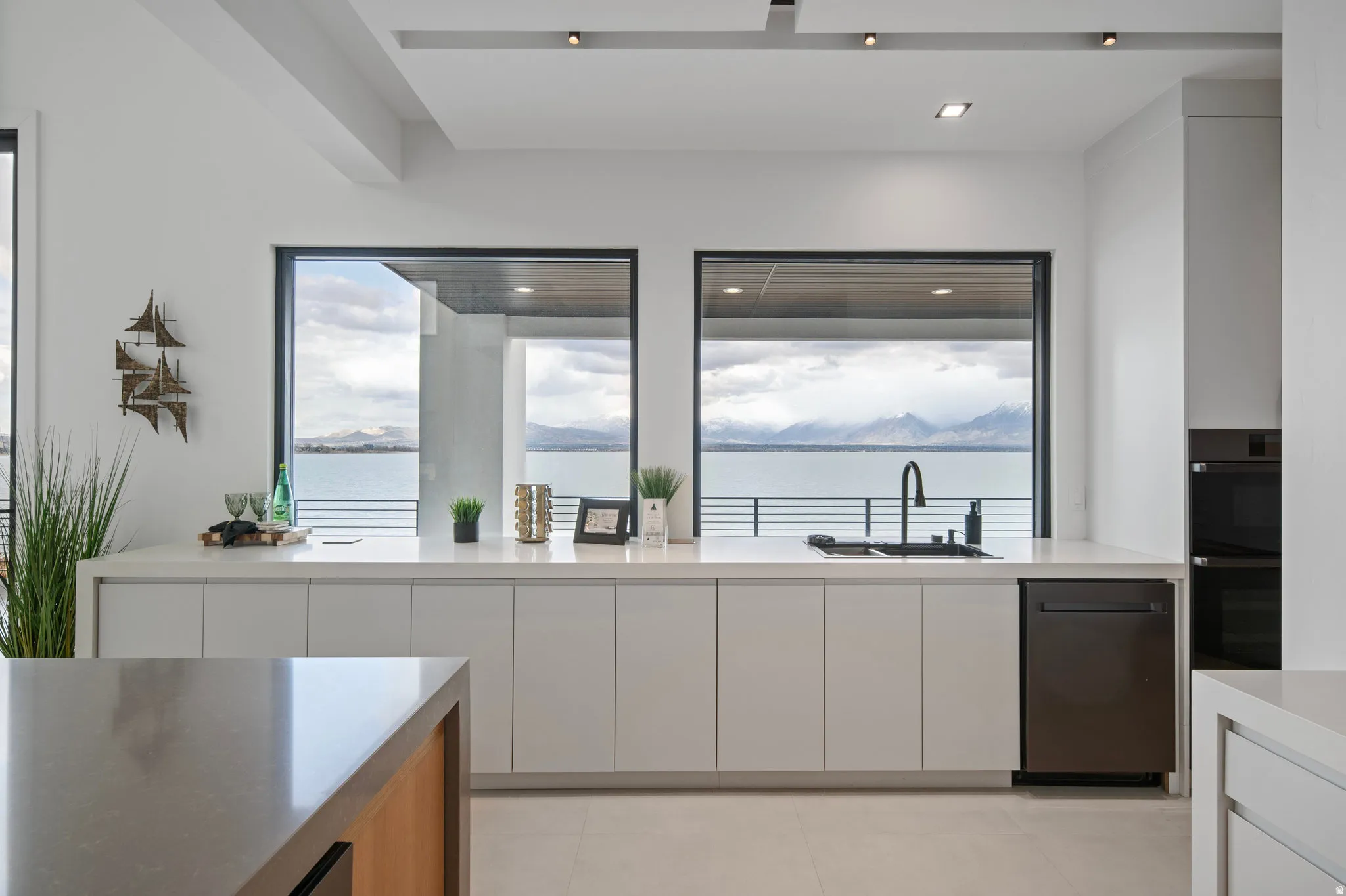 Contemporary kitchen featuring white cabinetry, light-toned countertops, a black sink with a matte black faucet, and integrated black appliances