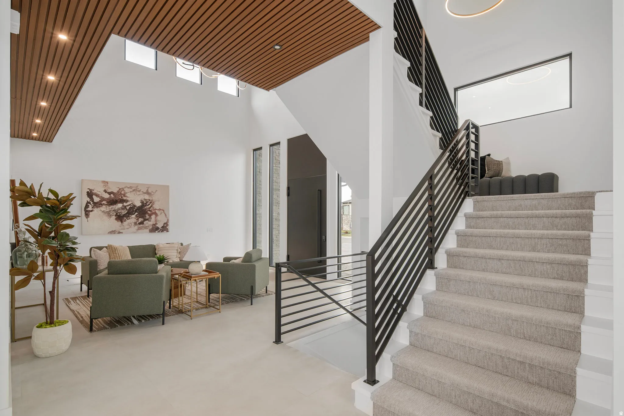 Vaulted ceilings with wood-slat accents, modern staircase with dark metal railings, large floor-to-ceiling windows, and light-colored flooring