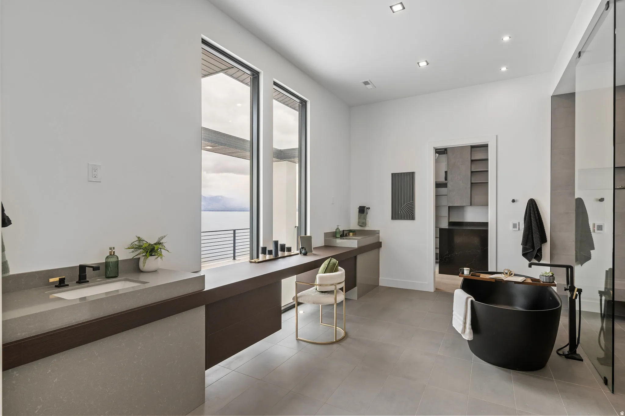Modern bathroom with large format tile flooring, a freestanding black soaking tub with a floor-mounted faucet, and two large windows offering extensive outdoor scenery