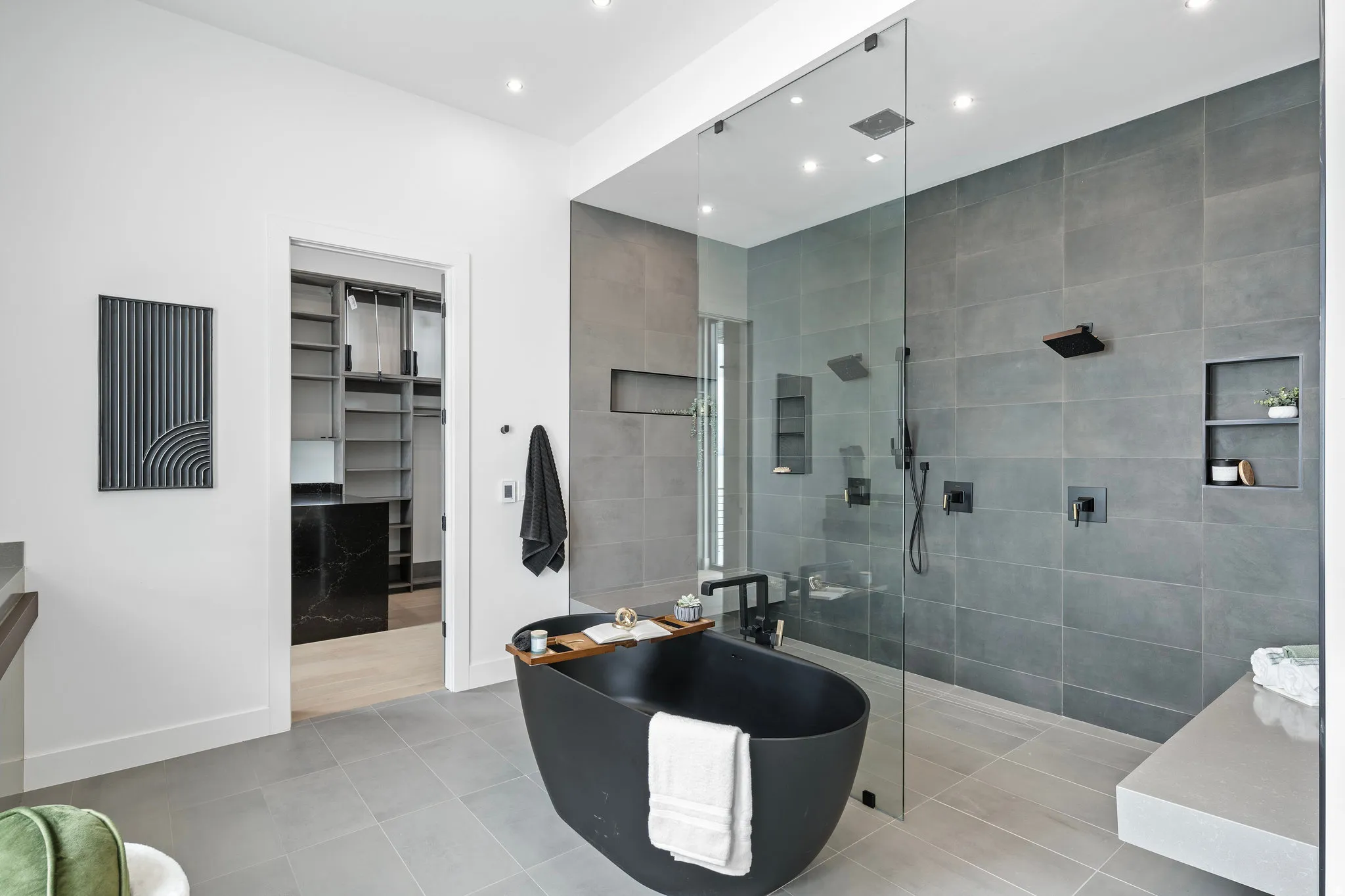 Spacious bathroom featuring a freestanding matte black soaking tub, frameless glass shower enclosure, dual showerheads, and recessed wall niches
