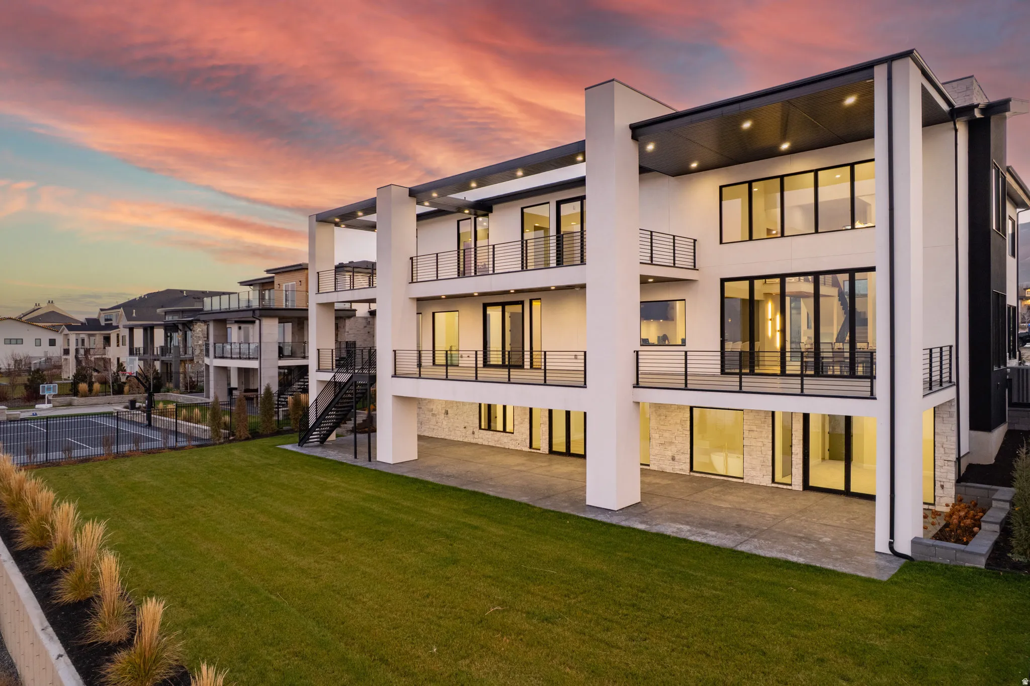 Contemporary exterior design featuring multiple balconies with black railings, expansive windows, a manicured lawn, and a paved patio area