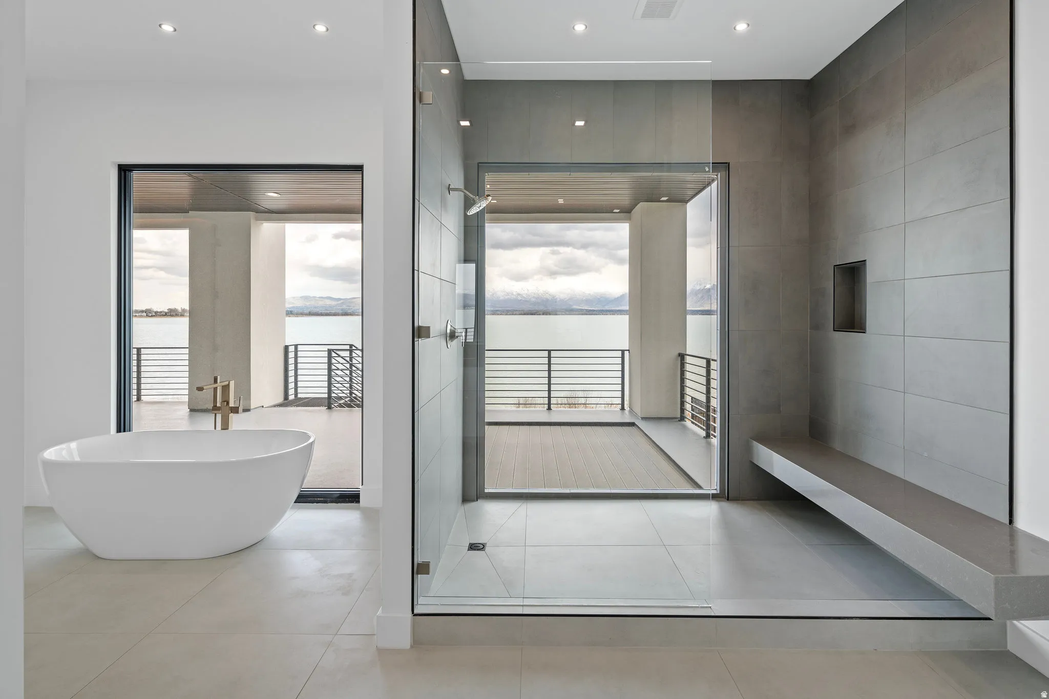 Freestanding soaking tub, walk-in shower with a built-in bench, large format tile, and floor-to-ceiling windows leading to an expansive balcony