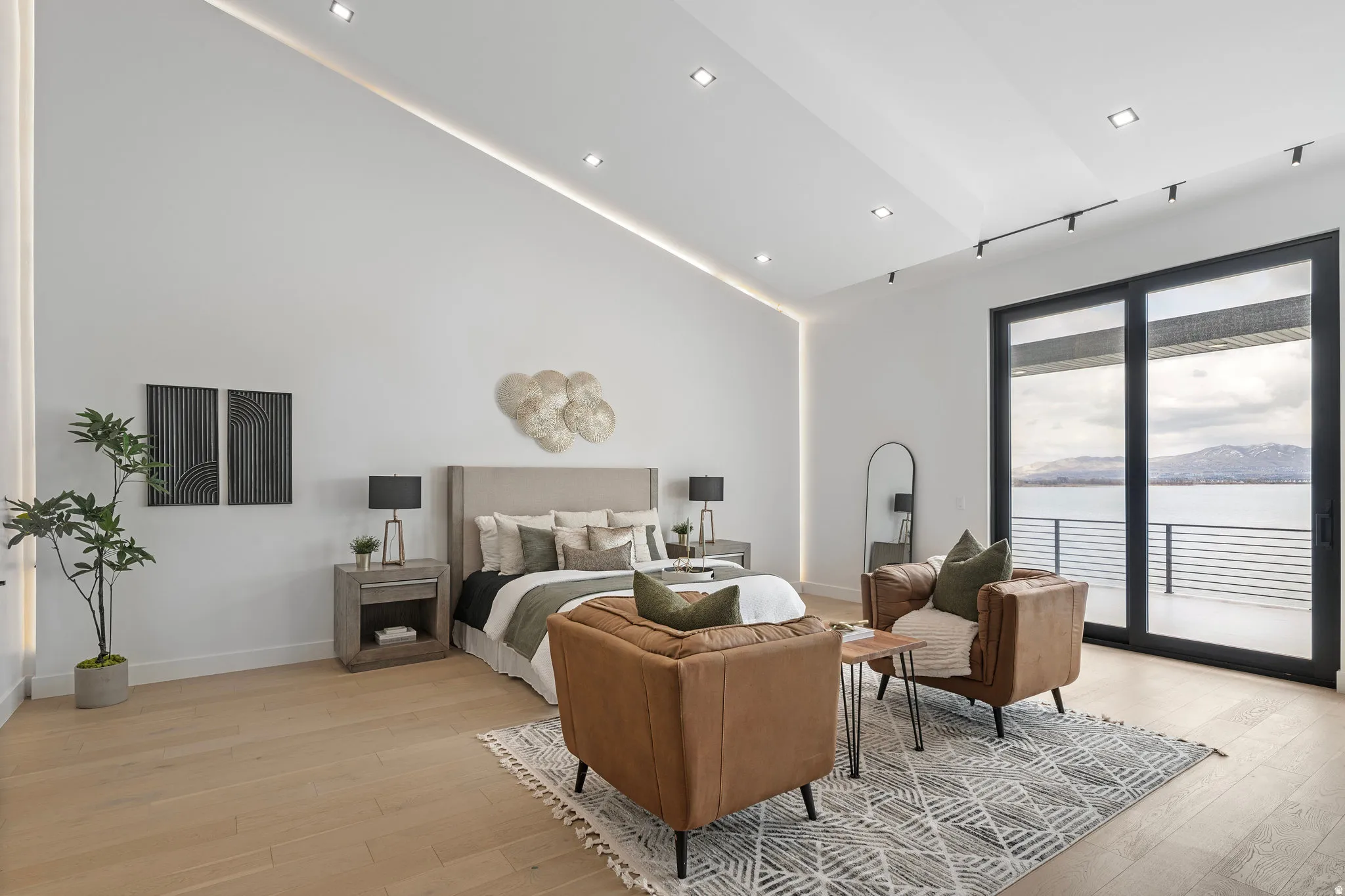 Vaulted ceiling with recessed lighting, light wood-finish flooring, sliding glass door access to an exterior balcony, and a scenic mountain and water backdrop