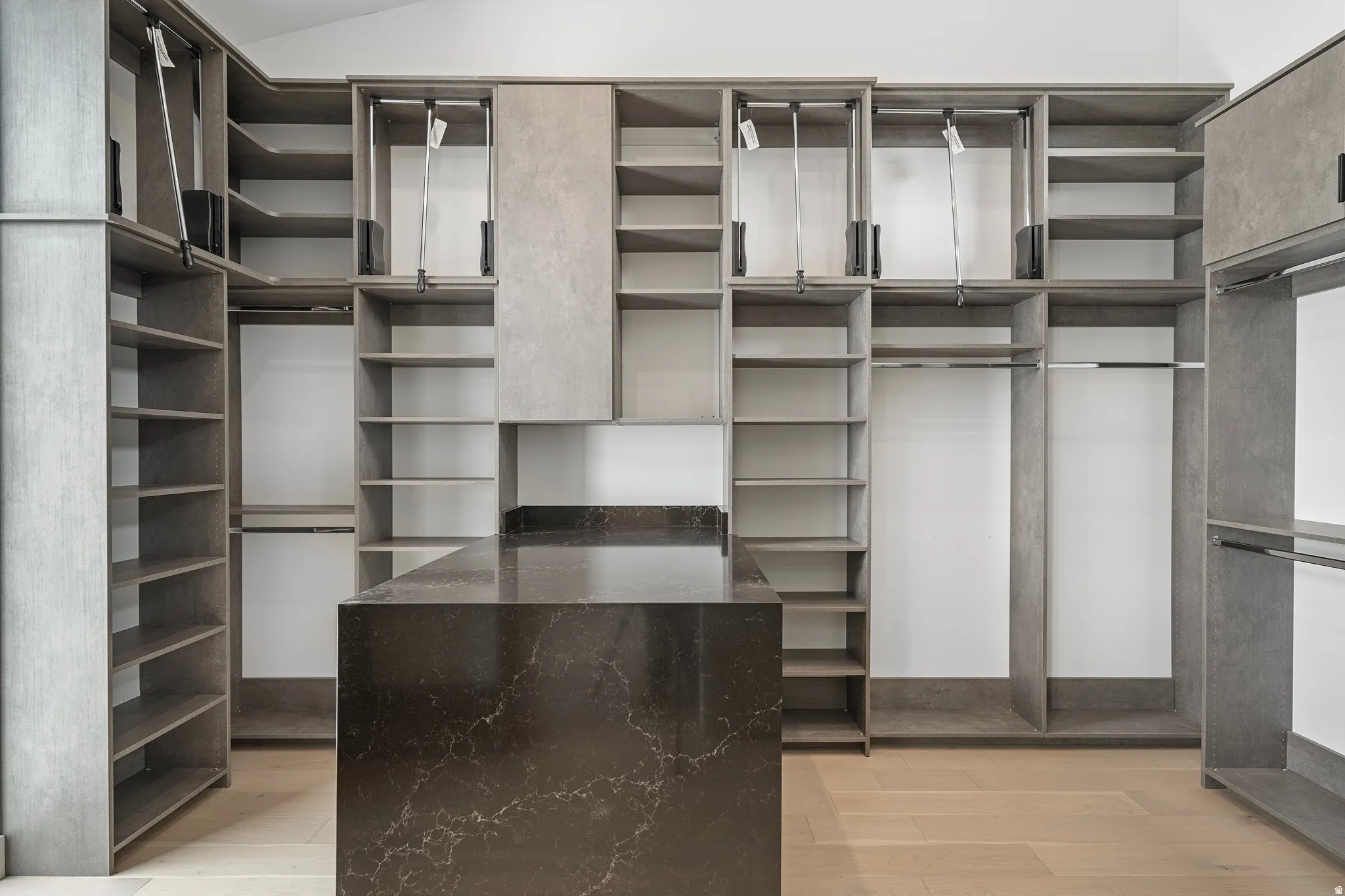 Integrated custom cabinetry with a central island, ample shelving, multiple hanging rods, and pull-down clothing racks
