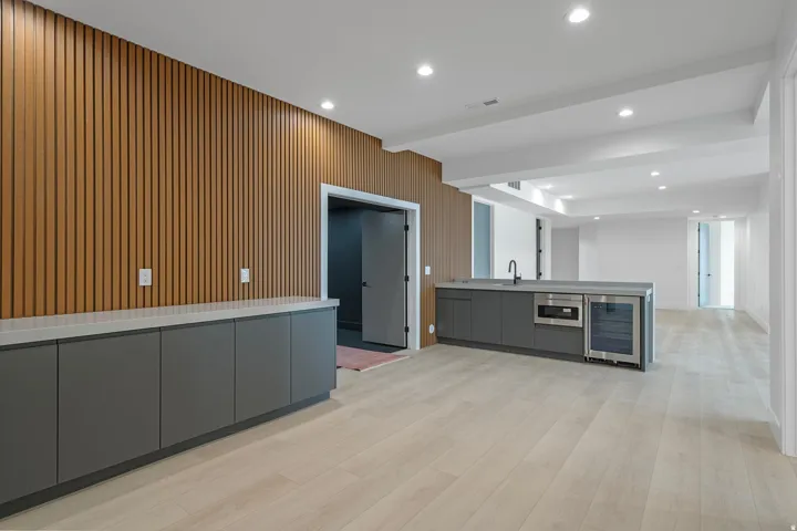 Wood-finish slat wall accent, recessed lighting, wood-finish flooring, built-in cabinetry with light-toned countertops, and an integrated beverage cooler