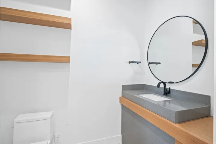Floating wood shelves, a circular black-framed mirror, and a contemporary vanity with an integrated sink and matte black faucet