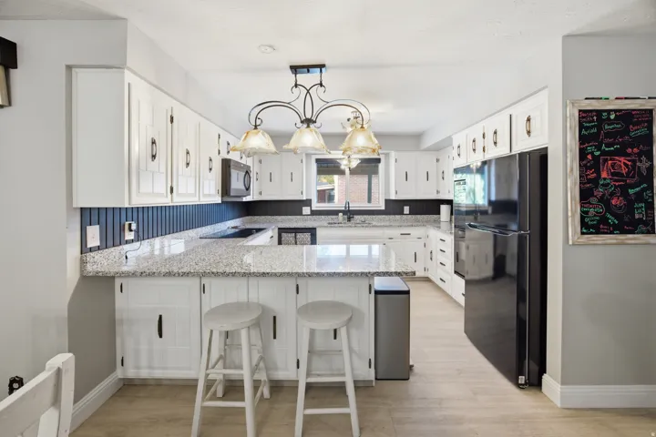 White cabinetry with black hardware, U-shaped countertops, central island with seating, dark-toned backsplash, and a built-in microwave