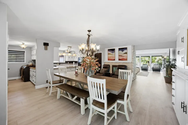 Light wood-finish flooring, built-in cabinetry, stone-clad fireplace, and a decorative chandelier