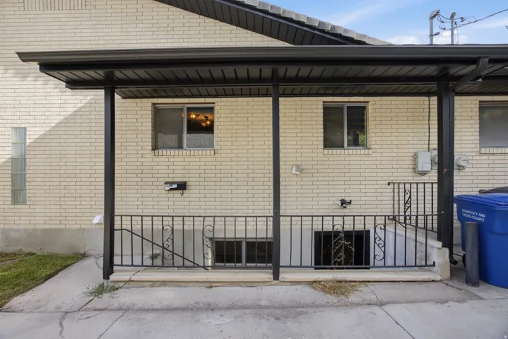 Light-colored brick exterior featuring a covered patio, black metal railing with scrollwork, and accessible basement windows