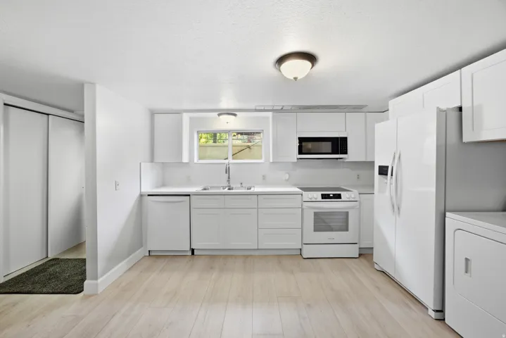 Kitchen featuring white cabinetry, light wood-finish flooring, white appliances, and a window above the sink
