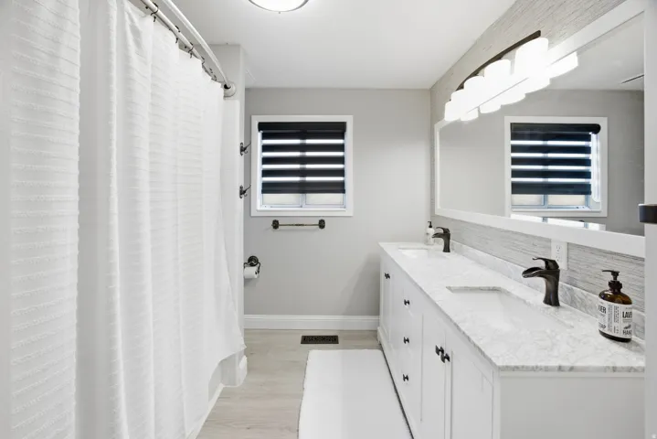 Double vanity with undermount sinks, stone countertops, dark bronze faucets, and a large wall-mounted mirror