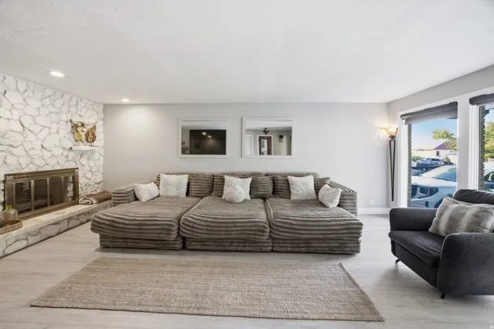 Stone-clad fireplace with a hearth, light wood-finish flooring, recessed lighting, and large windows with roller shades