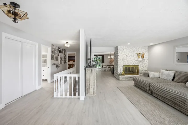 Light wood-finish flooring throughout, stone-clad fireplace with brass insert, white painted railing, built-in shelving, and recessed lighting