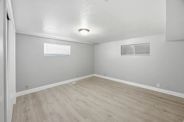 Neutral gray walls with wood-finish flooring, two windows with horizontal blinds, and a ceiling-mounted light fixture