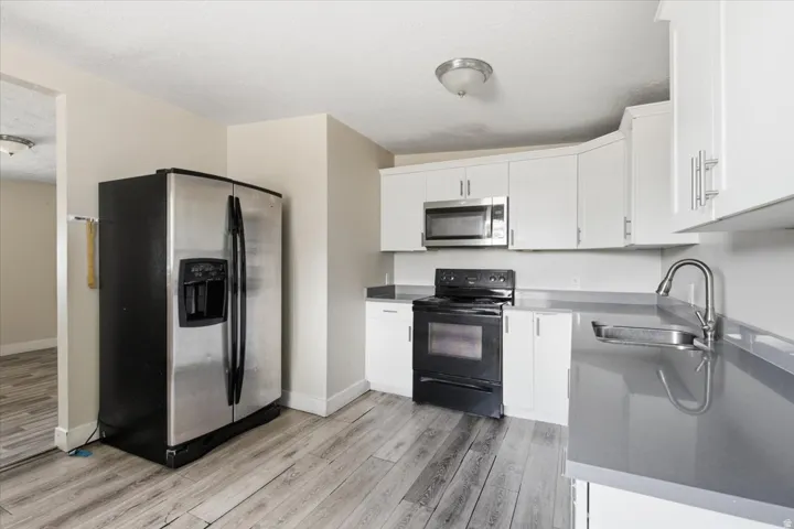 Kitchen featuring stainless steel refrigerator, white cabinetry with silver hardware, gray countertops, and wood-finish flooring