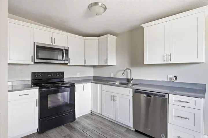 White cabinetry, stainless steel microwave, stainless steel dishwasher, black range, and wood-finish flooring