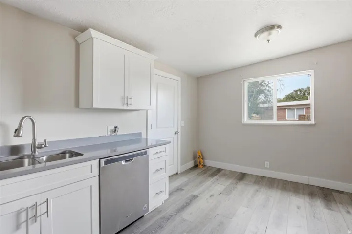White shaker cabinetry, stainless steel dishwasher, dual basin sink with gooseneck faucet, light gray countertops, and wood-finish flooring