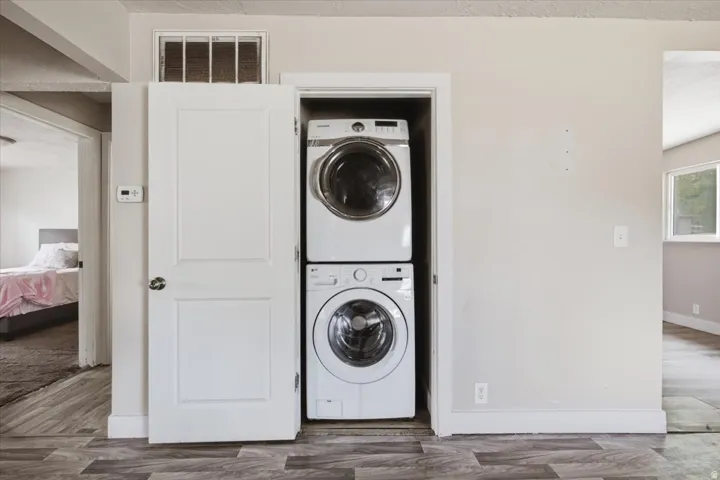 Built-in laundry closet with stacked appliances, paneled interior door, and wood-finish flooring